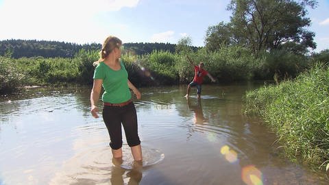 Eine Frau und ein Mann laufen barfuß durch einen Fluss.