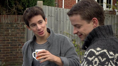 Zwei junge Männer sprechen miteinander. Der eine trinkt Kaffe.