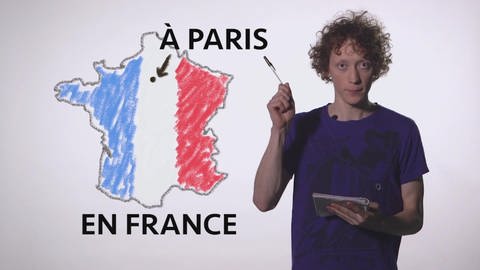 Ein junger Mann steht vor einer gezeichneten Frankreich-Karte und erklärt: "Les prépositions – Pays et villes"